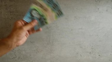 Avustralya dolarlarını üç tane 10 dolarlık banknotun sergilendiği beton bir arka fona karşı tutarak..