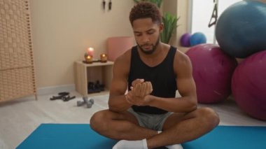 Spor salonunda egzersiz topları, mumlar ve spor aletleriyle bileğini uzatıp masaj yapan genç bir adam.