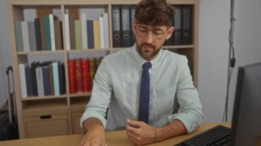 Ofisteki genç adam, kitaplıklar ve çalışma alanlarıyla çevrili akıllı telefonu kullanarak video görüşmesi yapıyor.