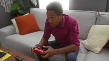 Adam rahat oturma odasındaki video oyununa odaklanmış. Kanepeye oturmuş, etrafı yastık ve bitkilerle çevrili..