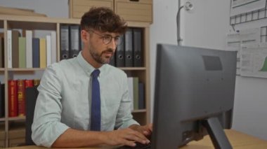 İş yerinde çalışan genç bir adam bilgisayarla uğraşırken gözlüğünü çıkardıktan sonra yorgun gözlerini ovalıyor.