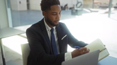 Video görüşmesi sırasında takım elbiseli ve elinde not defteri tutan genç bir adam.