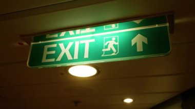 İçerideki yeşil arka plan ve yön okuyla aydınlatılmış parlak çıkış işareti güvenli bir ortamda acil çıkış yolunu sembolize ediyor..