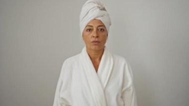 Havlu ve bornoz giymiş bir kadın parmaklarıyla kenarı işaret ederken şaşırdı. Şaşırmış bir ifade, ağzı açık, soyutlanmış beyaz bir arka planı var. Orta yaşlı İspanyol güzeli.