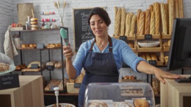 Fırında gülümseyen bir kadın ekmek ve pastalarla çevrili, önlük giymiş ve elinde maşayla yemek hazırlıyor.