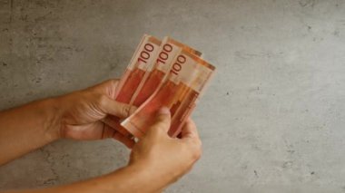 Somut bir arka planda Norveçli kron tutan eller, paranın ve parmakların detaylı bir yakın çekim görüntüsüne sahip 100 kronu gösteriyor.