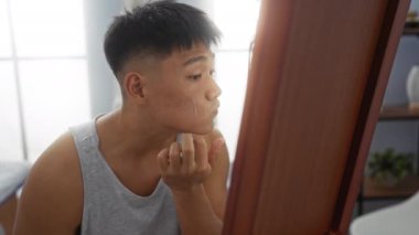 Genç adam güzellik ve rahatlama için spa sağlık merkezine aynaya bakarken yüzüne krem sürüyor..