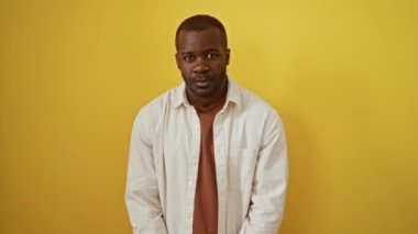 Öfkeli Afro-Amerikalı adam gömleğini giymiş, yumruğunu kaldırmış, öfkesini ve hüsranını izole edilmiş sarı arka planda gösteriyor. Öfkelenmiş öfke saldırganca ifade ediyor.