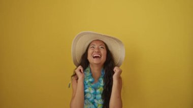 Kazanan! Yazlık şapkalı genç Çinli kadın ve Hawaii leyleği, sarı arka planda sevinçle yükselen kollarıyla başarıyı kutluyorlar.