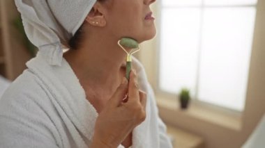 Kaplıcada yeşim taşı kullanan, bornoz giyen, sağlık merkezinde güzellik masajı yapan, parlak pencere ışığı olan bir kadın.