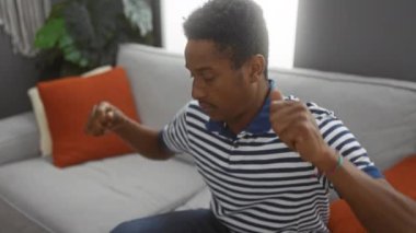 Oturma odasında rahat rahat rahat uzanan, rahat ve rahat bir şekilde, renkli yastıklar ve kapalı bitkilerle çevrili, çizgili gömleği olan genç bir adam..