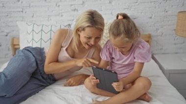 Anne ve kızı, yatak odasındaki rahat bir yatakta, tabletle etkileşime girerek evdeki kadın ve çocuk arasında yakın bir aile bağı olduğunu gösteriyor..