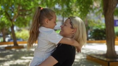 Anne ve kızı şehir parkında kucaklaşıp güneşli havalarda sevgi dolu bir anı paylaşıyorlar.