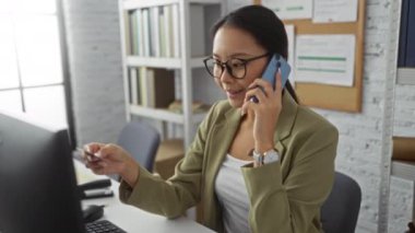 Ofis ortamında elinde kredi kartıyla konuşan bir kadın ciddi bir ifadeyle iş ya da finansal bir konuşmayı işaret ediyor.