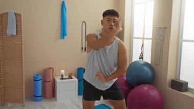 Genç adam Çin 'de bir sağlık spasında yoga minderleri ve arka planda egzersiz toplarıyla egzersiz yapıyor.