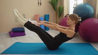 Spor salonundaki spor salonunda spor salonundaki spor malzemeleriyle çevrili yoga minderinde spor yapan bir kadın. Renkli spor topları ve paspaslar sağlık ve sağlığın önemini vurguluyor.