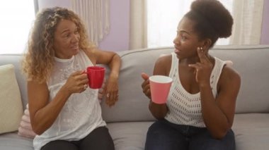 İki kadın bir apartman dairesinde oturmuş arkadaşça sohbet ediyor ve renkli bardaklardan içiyor.