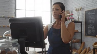 Fırında çalışan, önlük takan, telefonla konuşan ve bilgisayarında ekmek ve hamur işleri olan bir kadın.