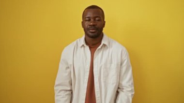Afro-Amerikalı adam ayakta dikiliyor ve kendine güvenerek işaret ediyor, sarı arka plan üzerinde başparmaklarıyla gülümsüyor, arkadan yakışıklı ve mutlu görünüyor.
