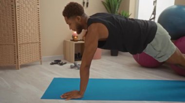 Spor salonunda spor aletleri ve mavi yoga minderiyle şınav çeken genç adam.