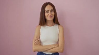 Pembe arka planda güven içinde poz veren genç bir kadın, uzun esmer saçlı sıradan bir tarz ve güzellik sergiliyor.