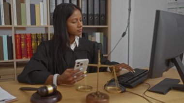 Ofisteki kadın yargıç bilgisayarda çalışıyor. Elinde tokmak ve terazili akıllı telefon var.