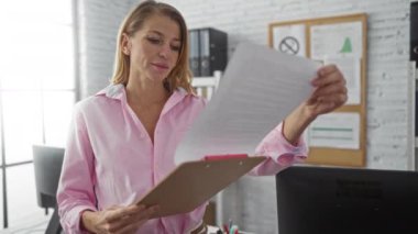 Parlak ofis ortamında, masa ve beyaz tahta içeren belgeleri inceleyen kadın, modern çalışma ortamını doğal ışıklandırma ve odaklanmış ifade ile örneklendiriyor..