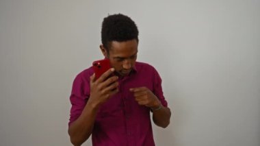 Kırmızı telefondan müzik dinleyen genç bir adam, beyaz bir arkaplanda izole edilmiş, günlük kıyafetlerle zevk ve konsantrasyon duygusu taşıyor..