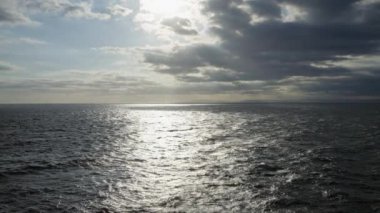 Okyanus manzaralı dramatik bulutlar ve güneş ışığı suya yansıyor, sakin bir manzara yaratıyor..
