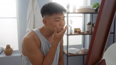 Genç bir adam spa odasında aynada kendine bakıyor, minimalist bir dekorla bir sağlık merkezinde düşünüyor ve gülümsüyor..