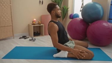 Sakin bir spor salonundaki paspasın üstünde yoga yapan genç bir adam. Spor yapmak için spor malzemeleri ve mumlarla..