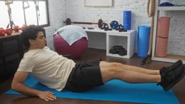 Genç, İspanyol bir adam, iyi donanımlı bir spor salonunda yoga minderinin üzerinde egzersiz yapıyor..