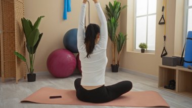 Spor salonundaki kadın paspasın üzerinde iç mekânlar ve egzersiz ekipmanlarıyla denge topları ve direnç antrenörleri de dahil olmak üzere sakin bir sağlık atmosferini vurguluyor..