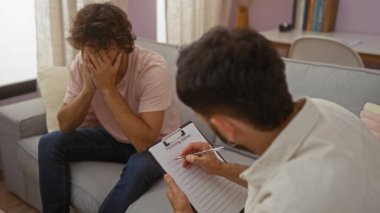 Başka bir adam evin içinde bir panoya yazı yazarken yüzünü kapatan bir adam. Muhtemelen oturma odasında terapi seansında.