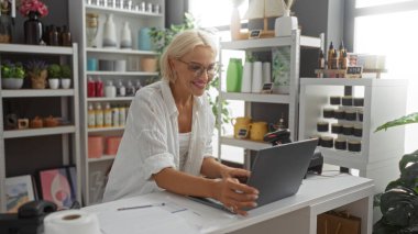 Dekorasyon mağazasında çalışırken gülümseyen kadın çeşitli dekoratif eşyalar ve bitkilerle çevrili..