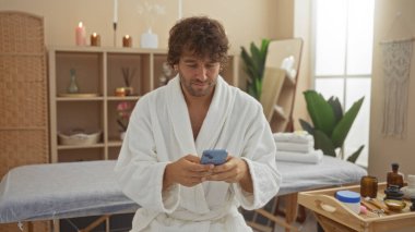 Kaplıca merkezinde beyaz bir bornoz giymiş genç bir adam ve bir akıllı telefon kullanıyor. Etrafı dingin bir salonun içinde sağlıkla ilgili şeylerle çevriliyken.