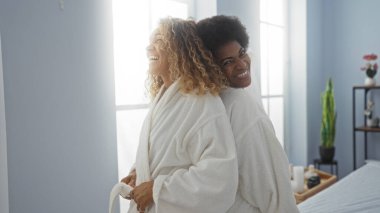 Beyaz cüppeli bir kaplıcadaki kadın arkadaşlar, birlikte neşeli bir anı paylaşıyorlar, huzurlu ve rahat bir atmosferi olan bir güzellik salonunda tasvir ediliyorlar..