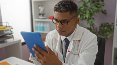 Genç İspanyol erkek doktor bir klinikte tablet hakkında bilgi okuyor.