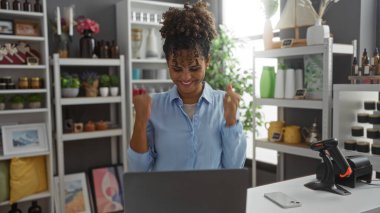 Ev dekorasyonu mağazasında arka planda dekoratif eşya raflarıyla kutlama yapan bir kadın.