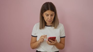 İzole edilmiş pembe arka planda duran akıllı telefon kullanan bir kadın esmer saçlı, genç ve çekici bir İspanyol kadını resmediyor.