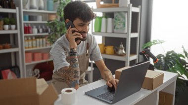 Diz üstü bilgisayarda çalışan ve iç dekorasyon mağazasında telefonla konuşan sakallı genç bir İspanyol.