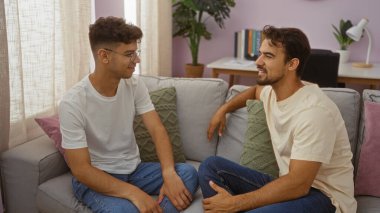 İspanyol bir baba ve oğlu sıcak bir oturma odasında oturup sevgi dolu bir sohbete girişiyor, aile bağlarını ve konforlu bir yuva ortamındaki bağlantıları vurguluyor..