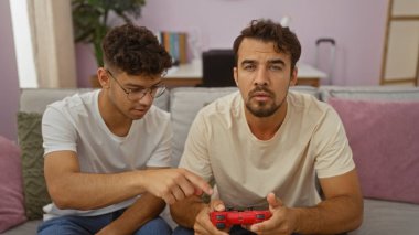 Baba ve oğul, rahat bir oturma odasındaki kanepede oturup video oyunları oynayarak, modern bir apartman dairesinde sevgi ve yakınlık göstererek vakit geçiriyorlar.