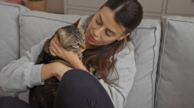 Genç bir İspanyol kadın oturma odasında bir kediye sarılıp ev kedisiyle sıcak bir ortam yaratıyor..