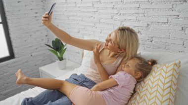 Anne ve kızı yatak odasında video görüşmesi yapıyorlar, telefonla yatağa uzanıyorlar, evde bir bağ kuruyorlar.