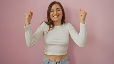 Genç ve çekici bir sarışın kadın, pembe bir arka plan duvarında izole edilmiş, coşkulu yumruklarıyla kutlama yapıyor..