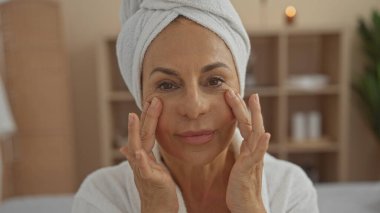 Kafasına havlu sarılmış, güzellik ve sağlık için yüz masajı yapan olgun bir kadın..