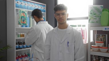 Bir eczanenin içinde birlikte çalışan İspanyol eczacılar, etrafları ilaç ve ürünlerle çevrili, profesyonel ve işbirlikçi bir ortam yakalıyorlar..