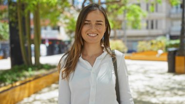Güneşli bir günde şehir parkında gülümseyen çekici genç bir kadın..