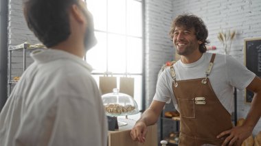 Erkekler sıcak bir fırında dost canlısı bir fırıncı ve gülümseyen bir müşteriyle sohbet ediyorlar.